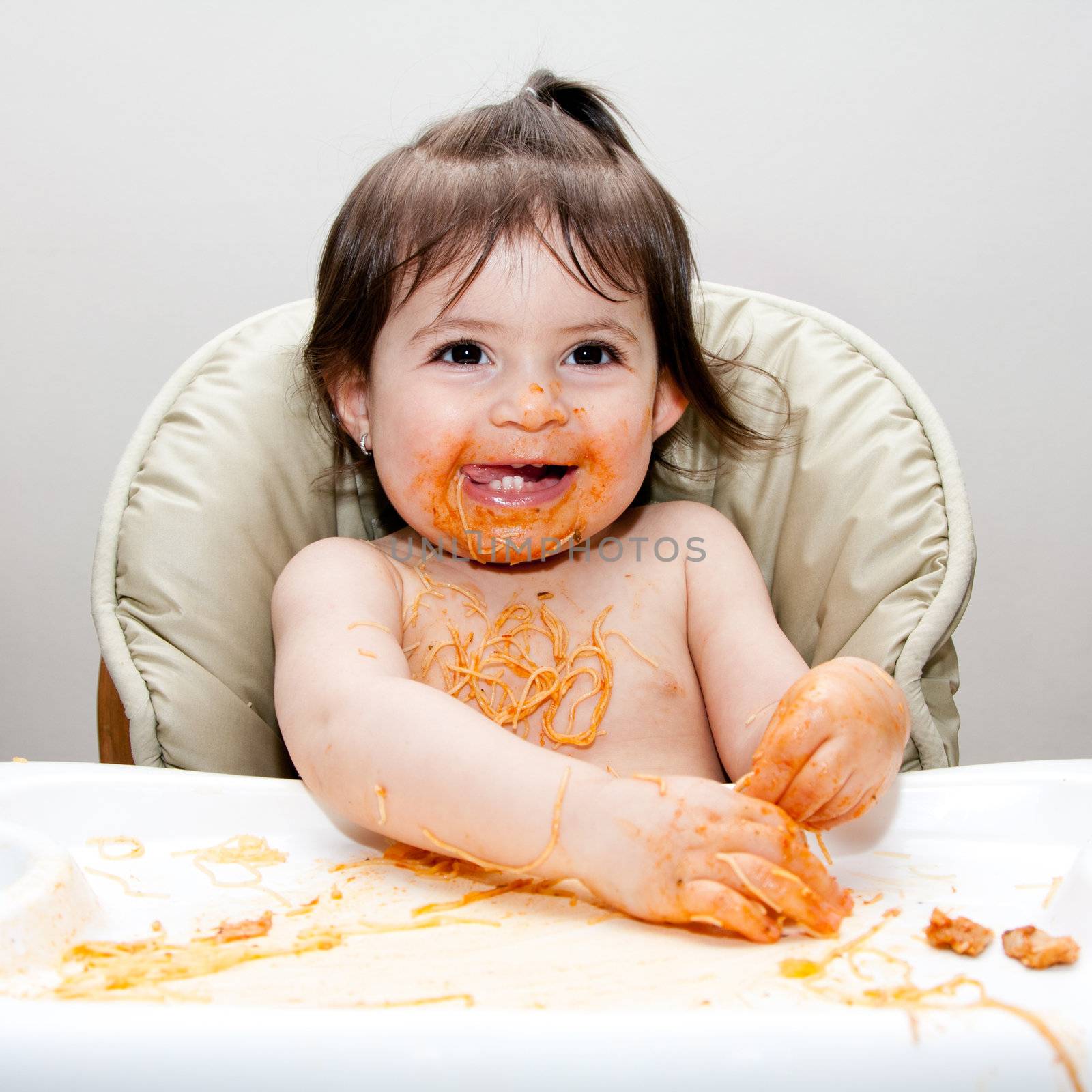 Happy baby having fun eating messy covered in Spaghetti Angel Hair Pasta red marinara tomato sauce.