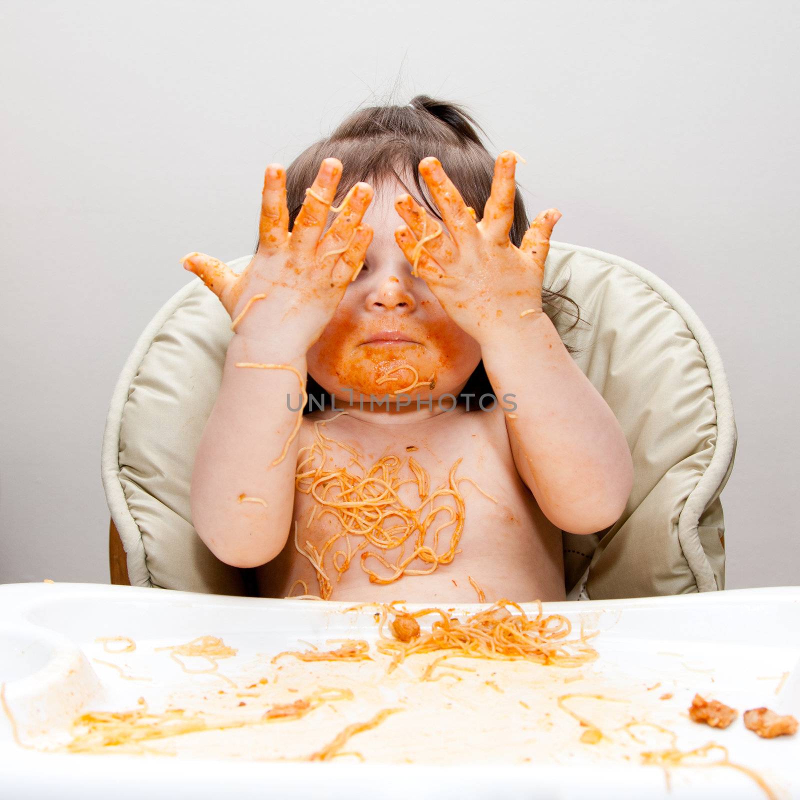 Happy baby having fun eating messy showing hands covered in Spaghetti Angel Hair Pasta red marinara tomato sauce.