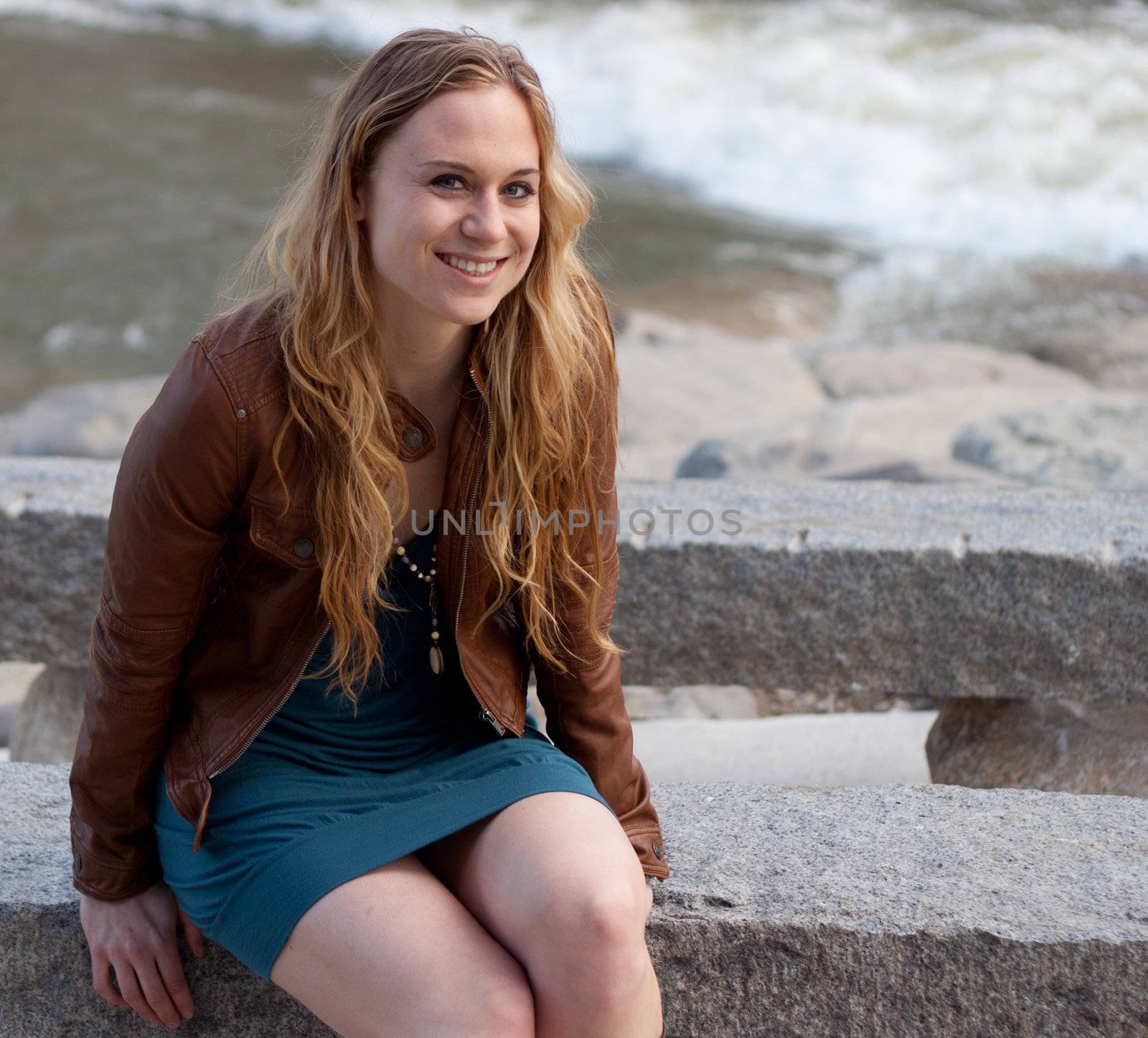 A beautiful friendly girl sits down on a stone bench by the water.