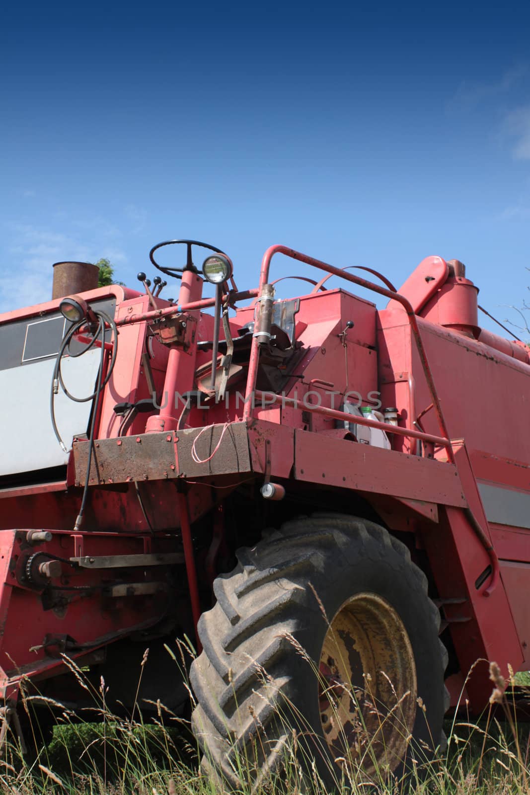The front end of a red combine harvester machine stationary in a farm field in rural Wiltshire, England, set against a blue summer sky.