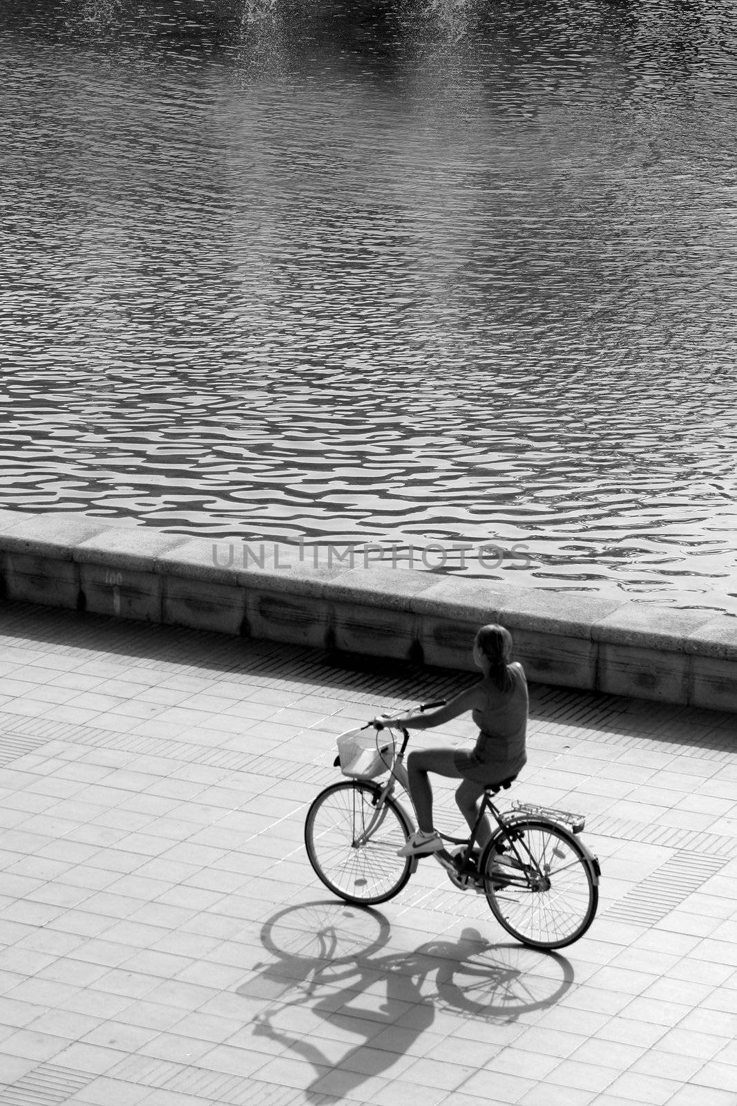 backlit silhouette of girl riding a bike close to park lake, black and white