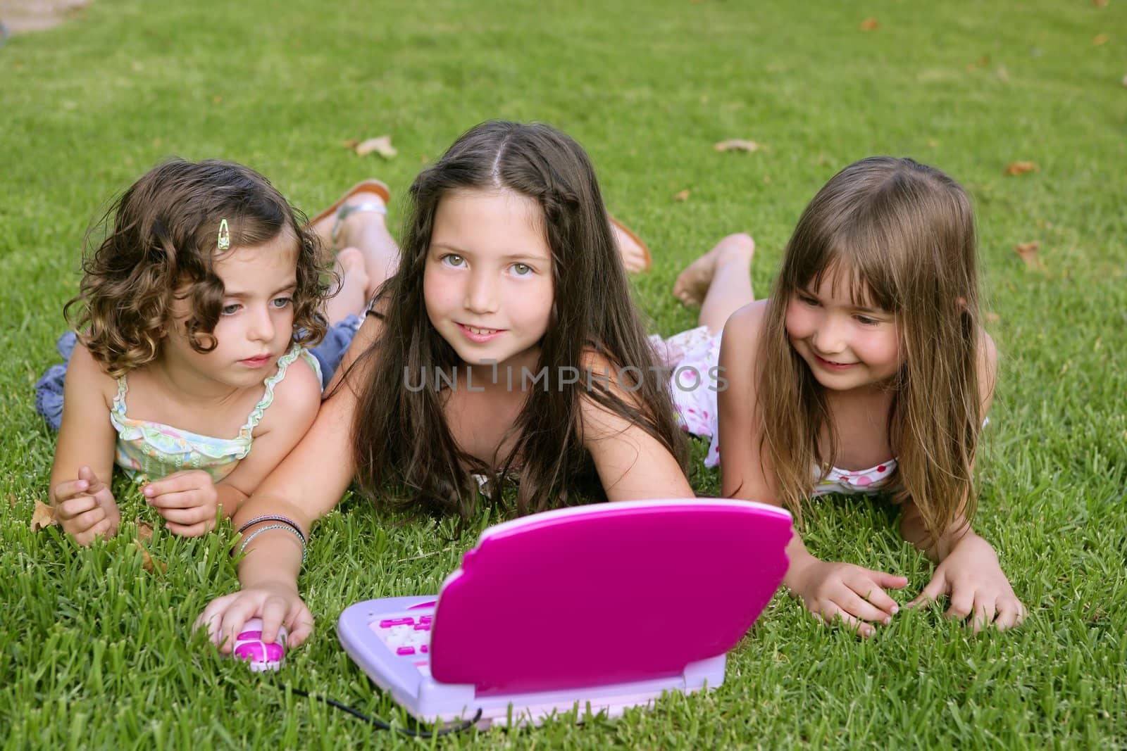 Three little girl playing with toy computer in grass by lunamarina