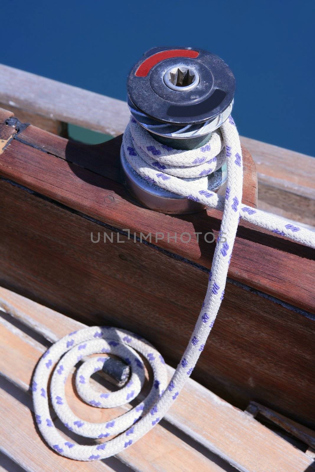 Marine rope and winch over wooden deck and blue summer sea