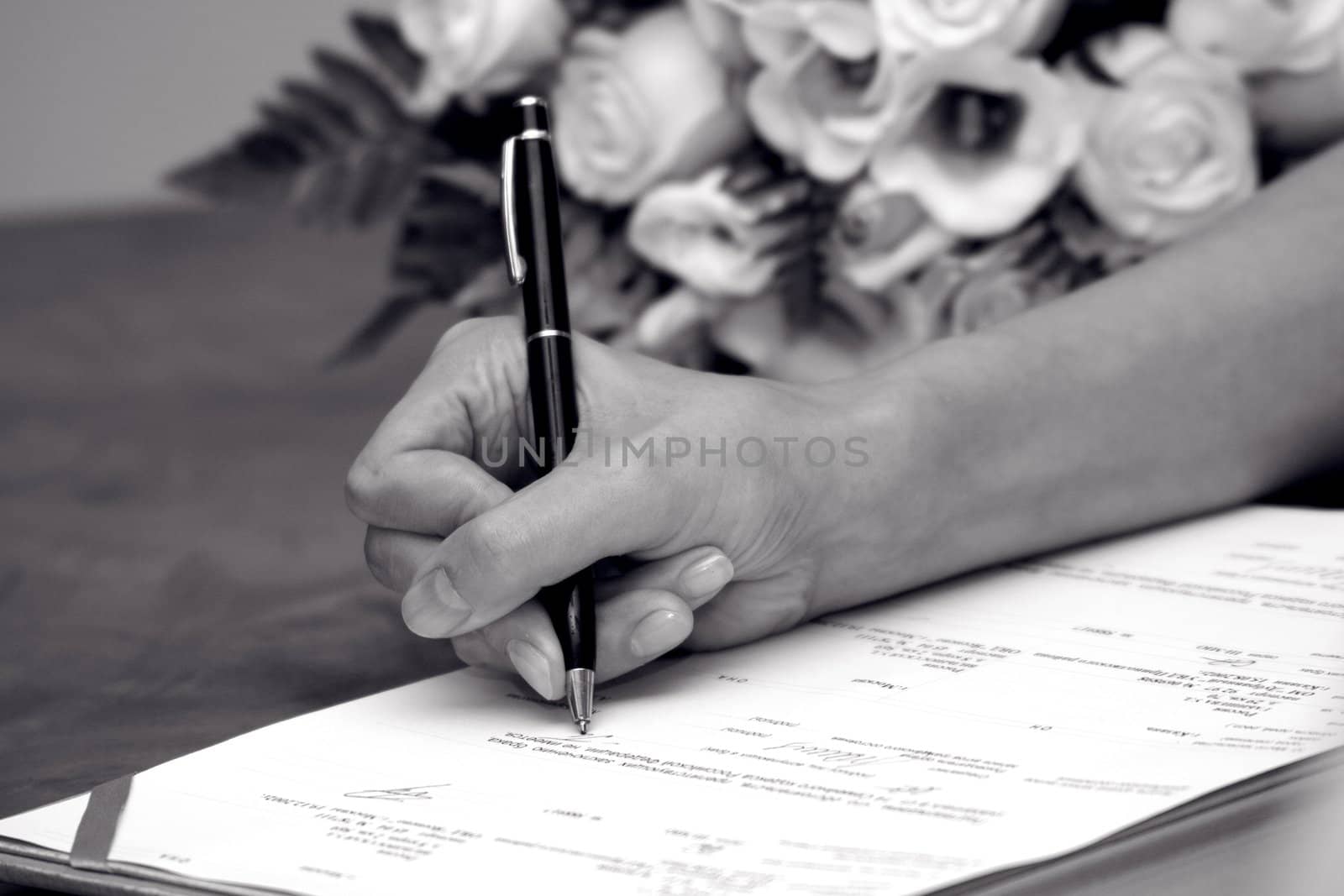 Woman's hand signing documents near a wedding bouquet