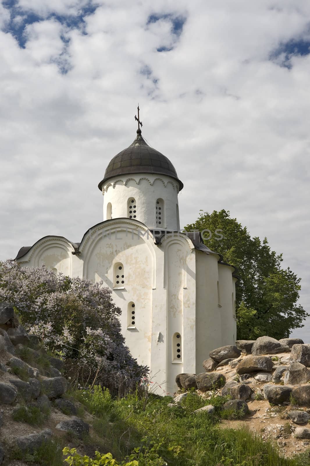 White russian church with blossoming lilac and old fortress ruins 