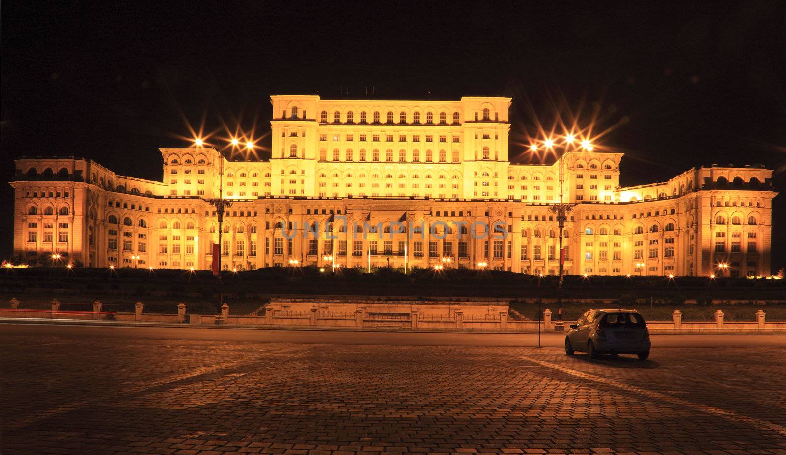 Night image of a car in front of the The Palace of the Parliament, also known as The People's House in the Cheauchesku's era, in Bucharest,Romania. The Palace is the world's largest civilian administrative building, The Pentagon being the largest overall. It is the most expensive and heaviest building in the world.