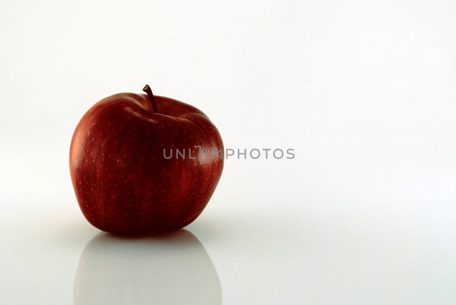 Red apple on reflective background against white with copy space