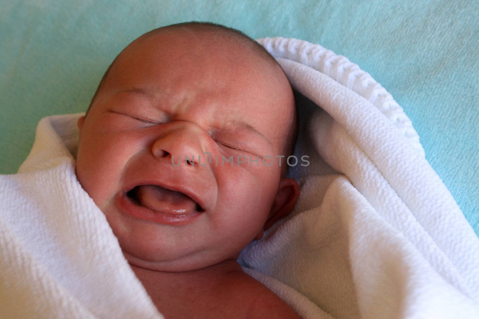 Week old baby boy wrapped in a blanket, crying early in the morning