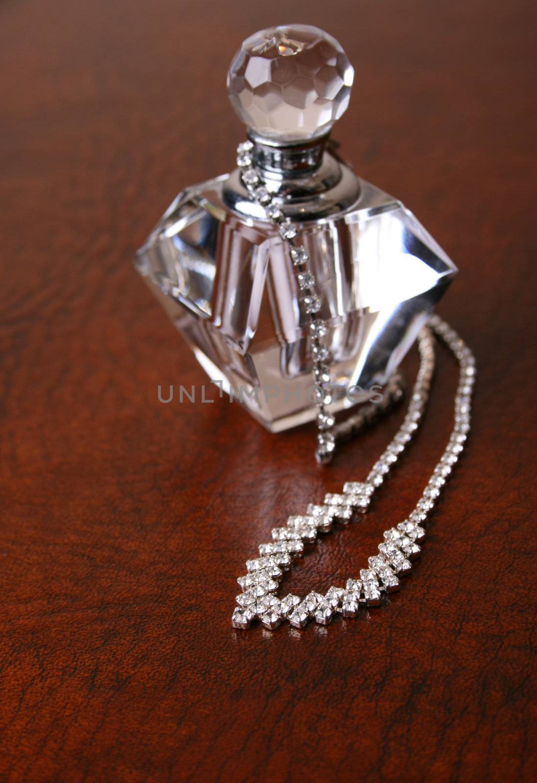 Diamond necklace on a leather surface next to an empty perfume bottle