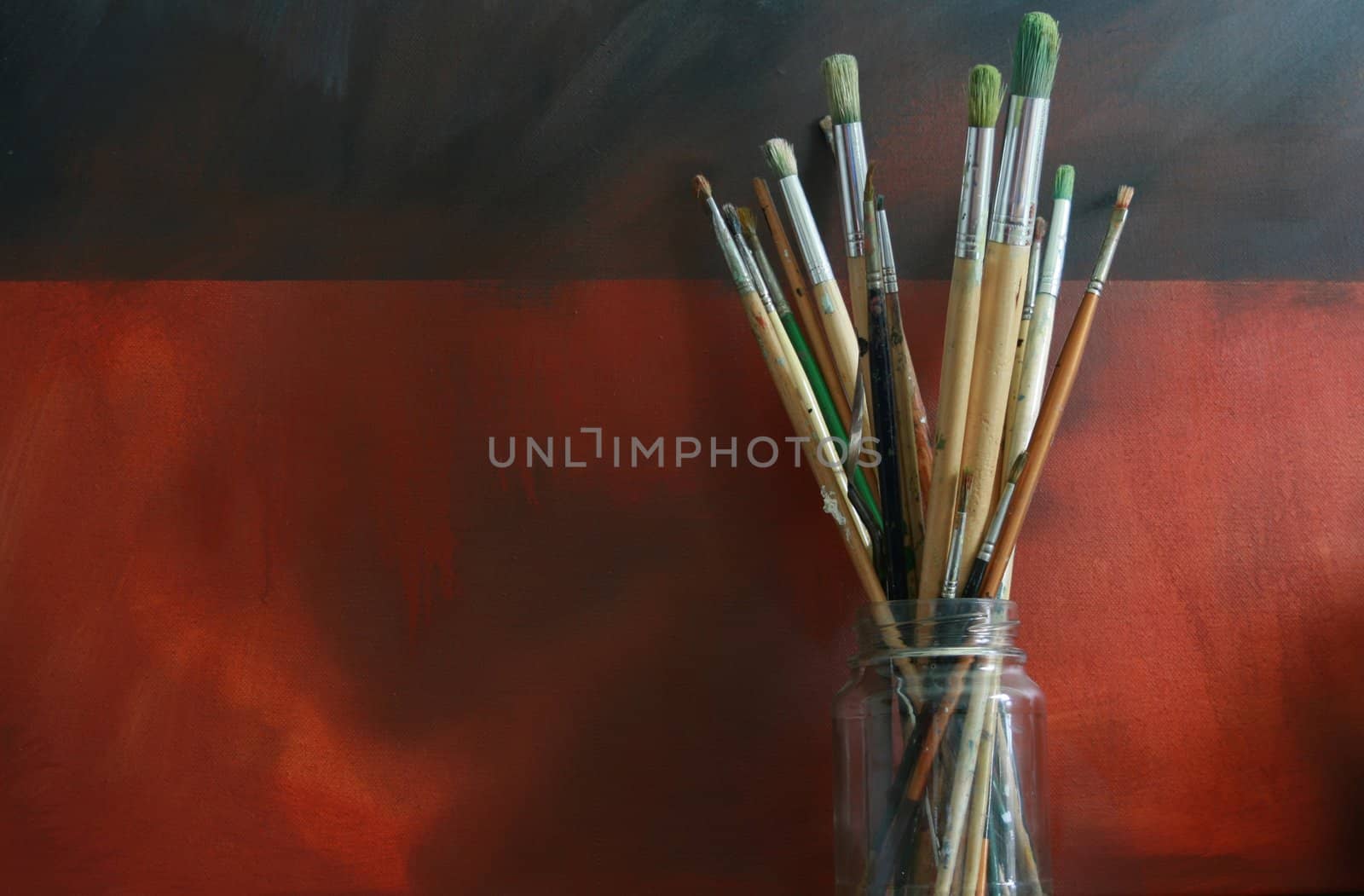 A jar of artists brushes set against a grunge styled backdrop. Set of centre to main image.