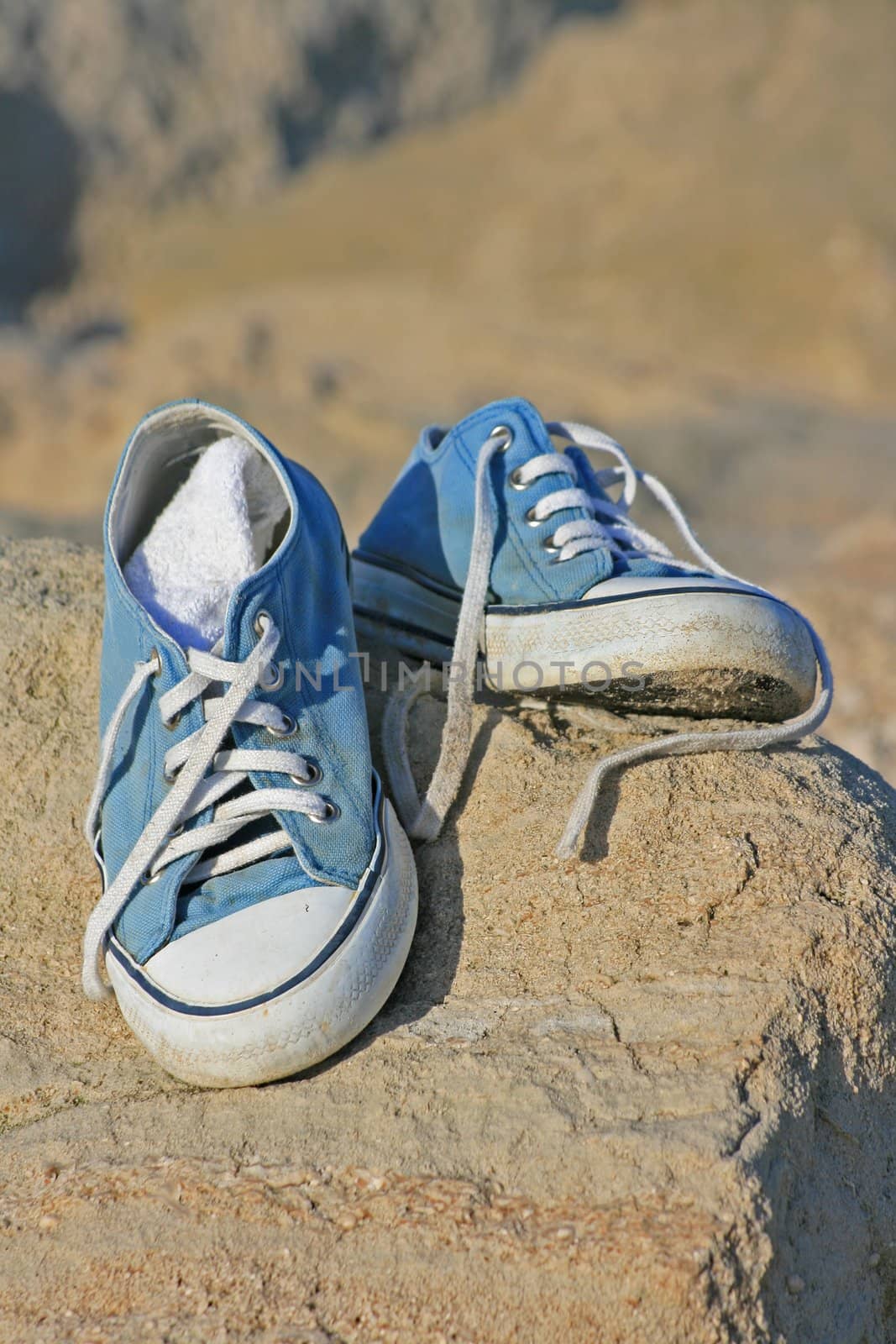 A pair of trainers/gym/beach shoes on top a rock at the beach.