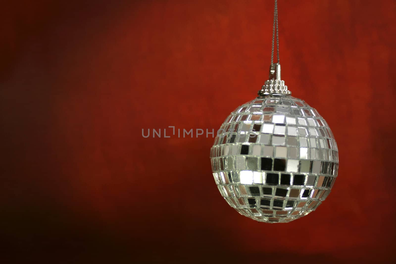A hanging glitter ball christmas decoration, set on a red grunge styled background.