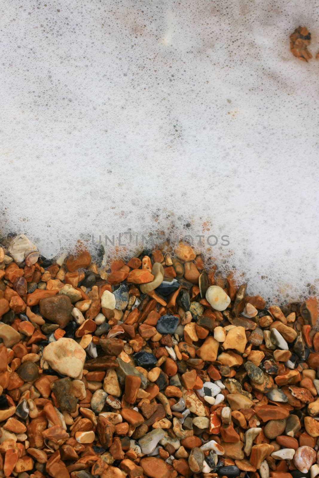 Background image of pebbles on a beach with sea foam wash emerging from top of image. Location in Christchurch, Dorset UK.