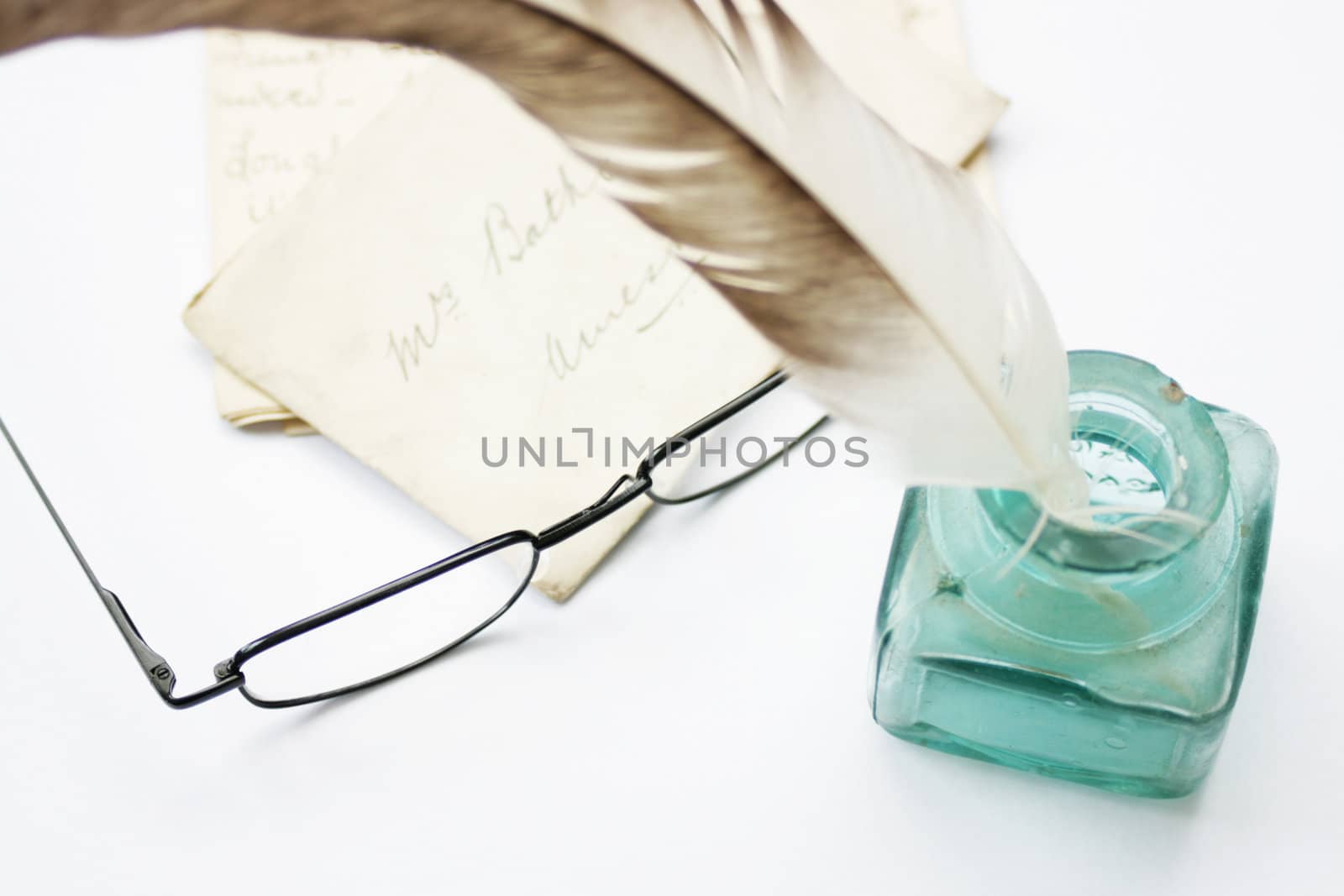 A feathered quill pen standing in a glass ink pot with old hand written letters behind, set on a white background
