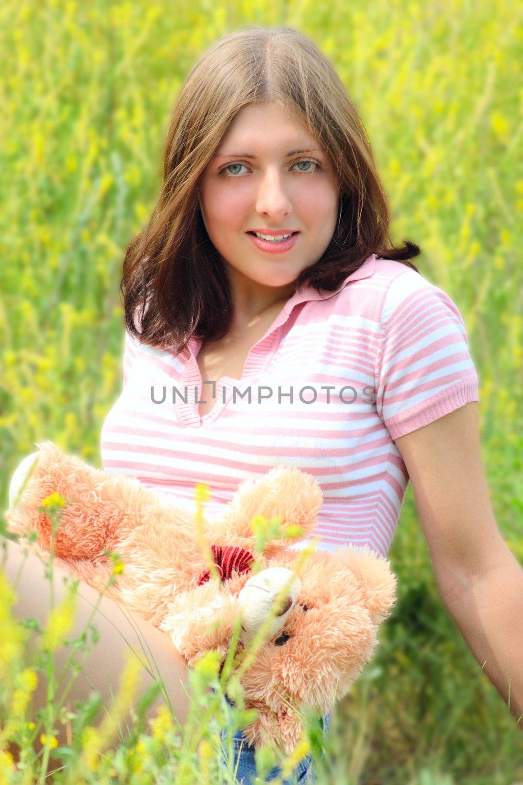 The girl sitting on a summer meadow with a toy bear cub