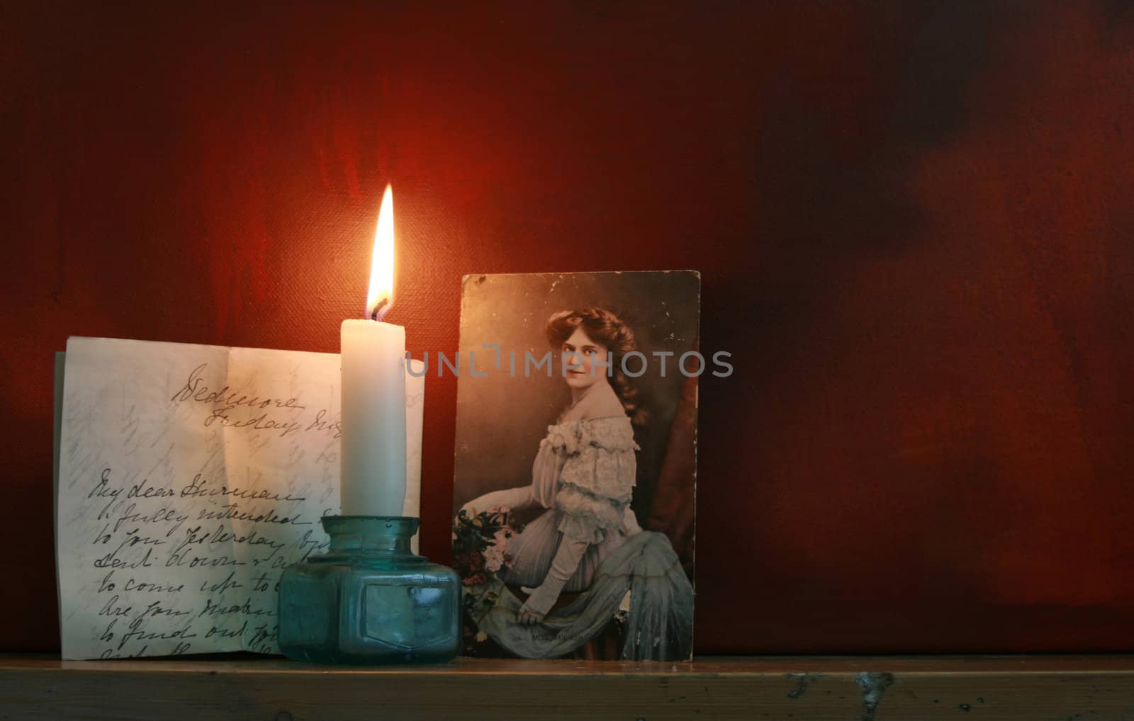 Victorian Love letters set top a mantle piece with a candle against a dark red grunge styled background. Mood evocative.