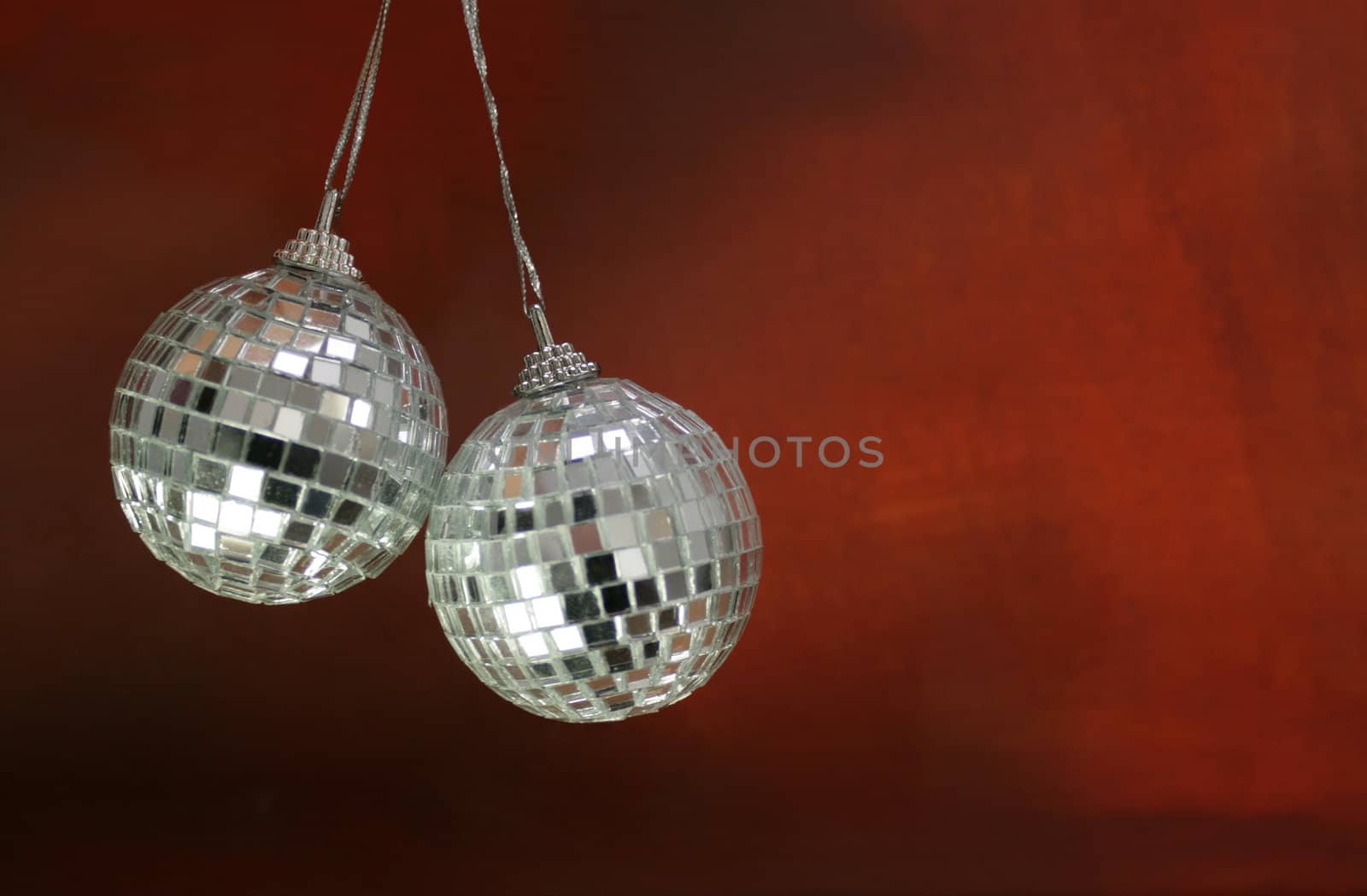 Two hanging glitter ball christmas decorations, set on a red grunge style background.