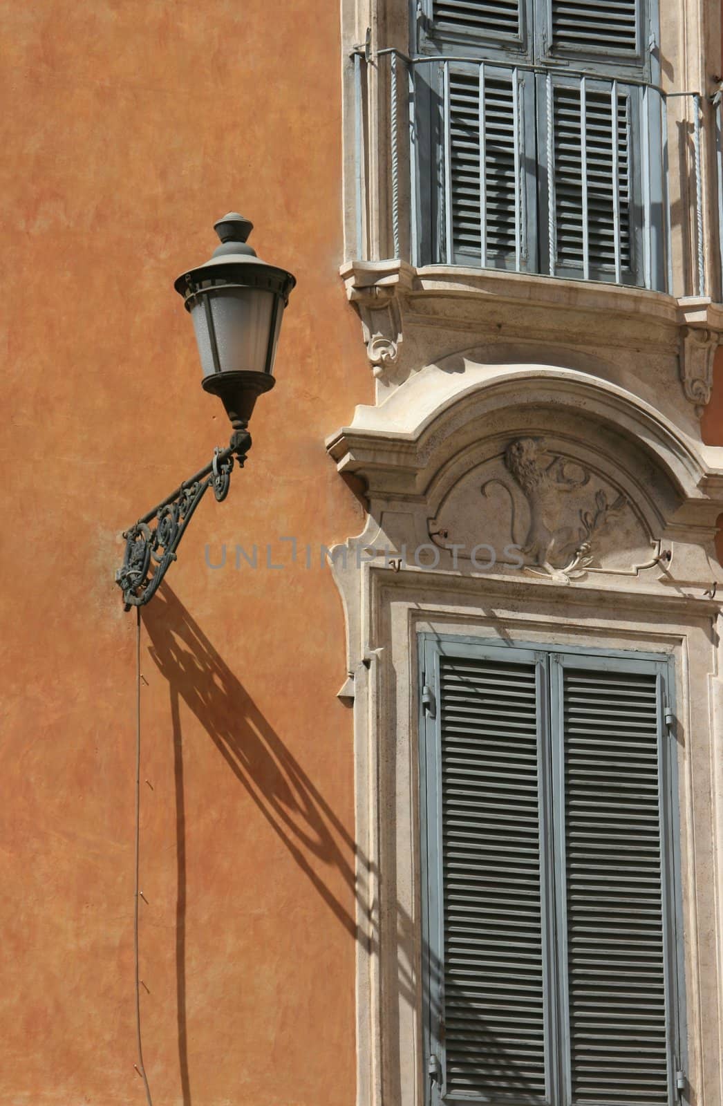 Detailed shot of an italian architecture found in Rome, Italy. Powder blue shuttered windows on a terracotta plaster wall with exterior light casting a shadow.