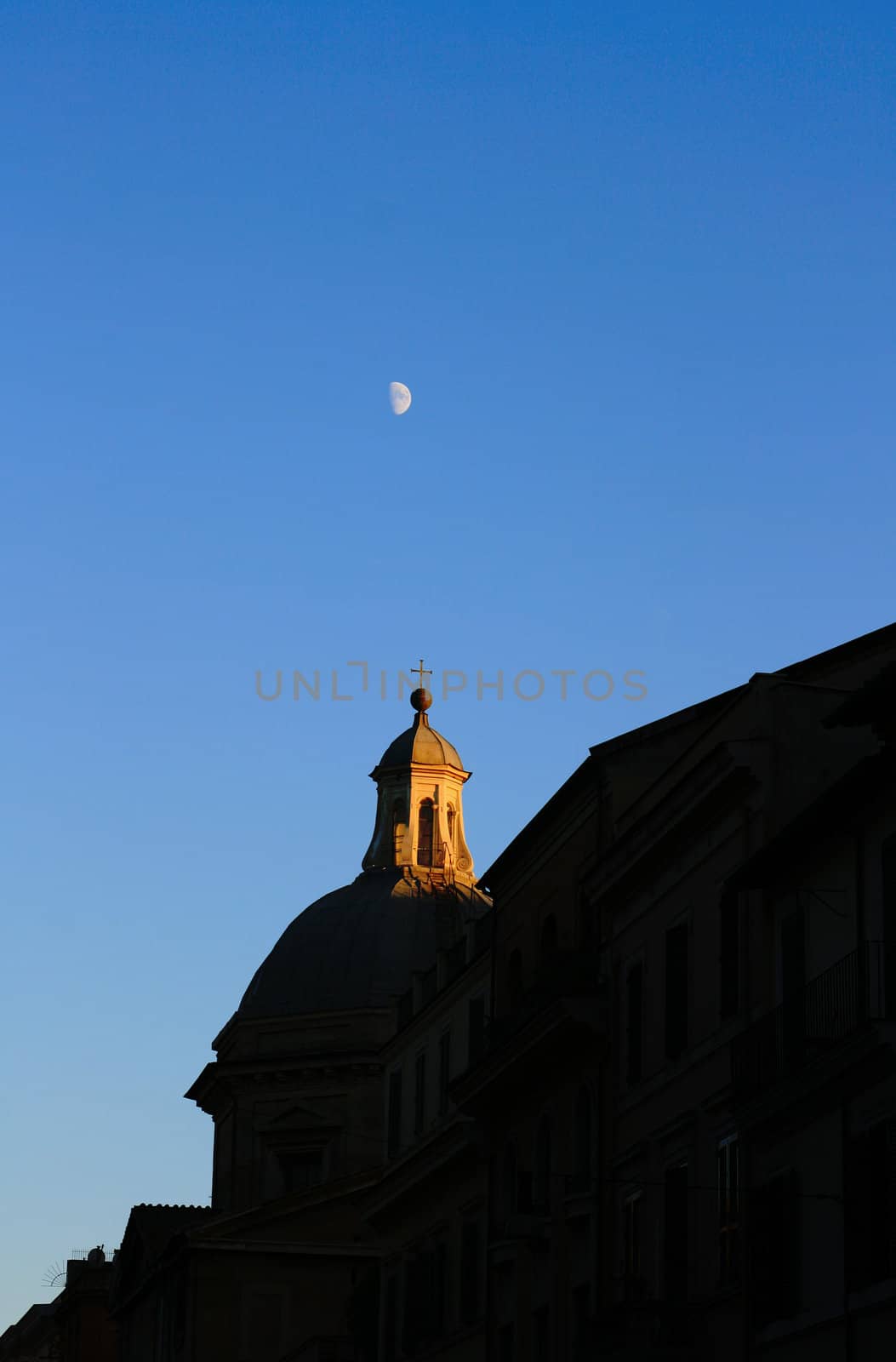 Sunset skyline over Rome, Italy with moon visible against a crisp blue sky.