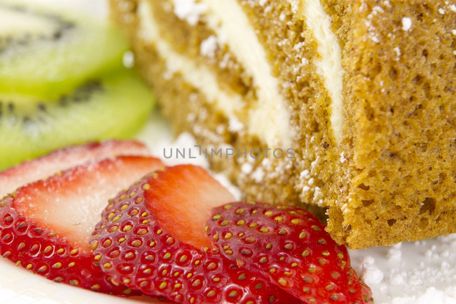 A rolled cake garnished with sliced strawberries and kiwi fruits.