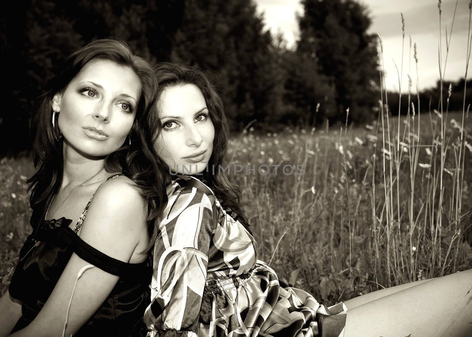 Two sensual girls sitting closely in the grass