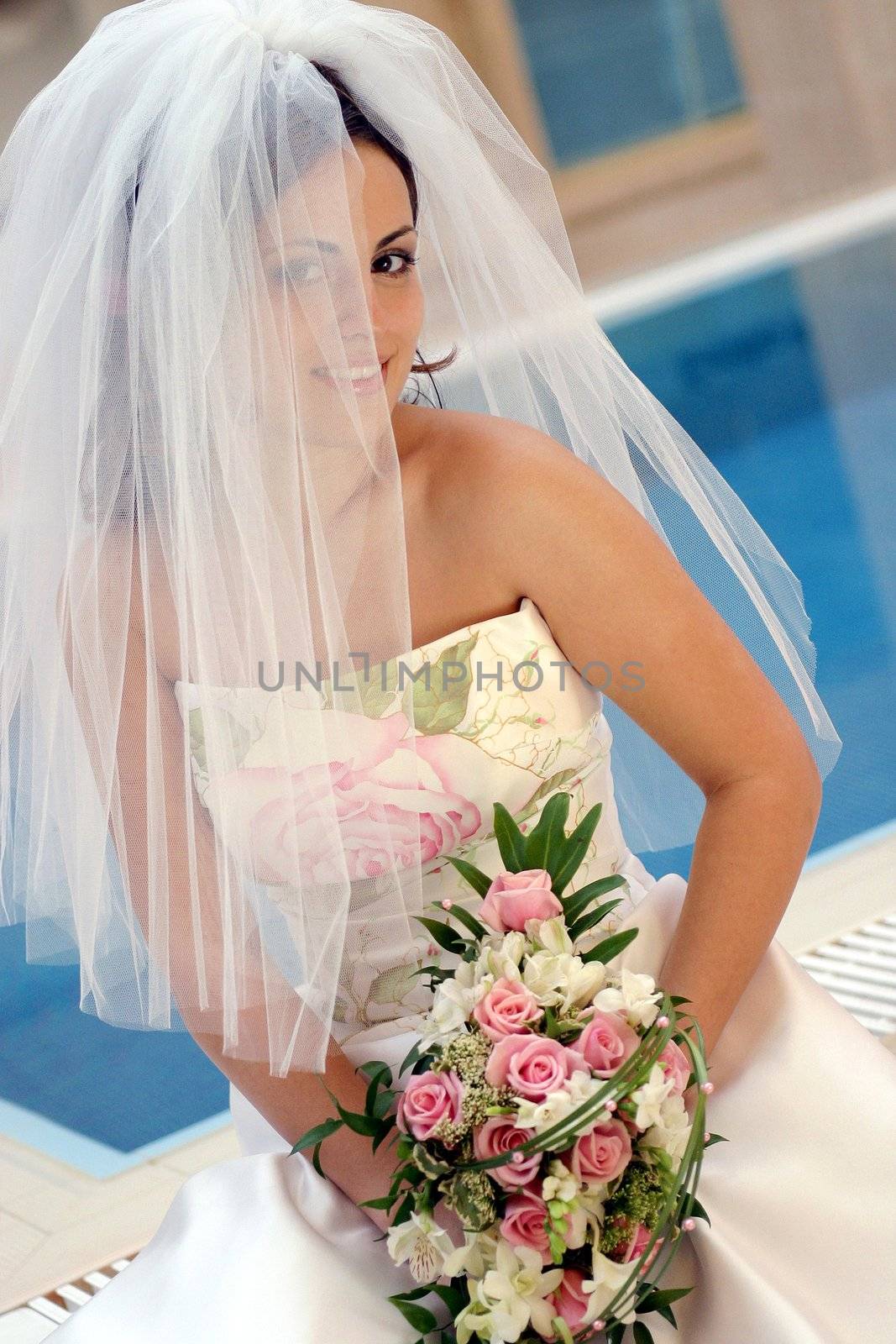 Smiling young bride wearing veiled white dress holding bouquet of flowers.