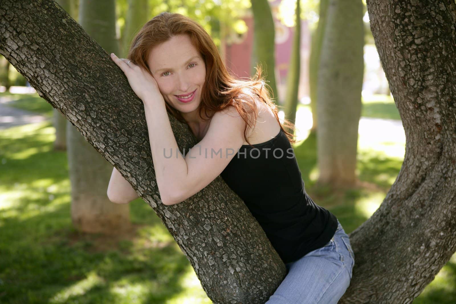 Beautiful redhead woman sitting on the park tree with smile