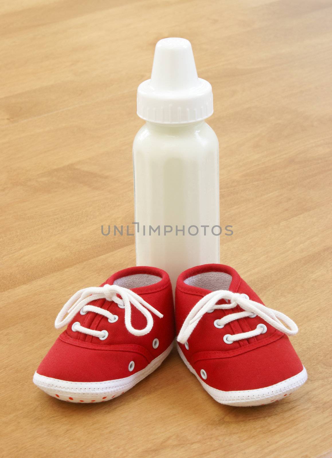 A baby bottle and a pair of shoes are sitting on a table.