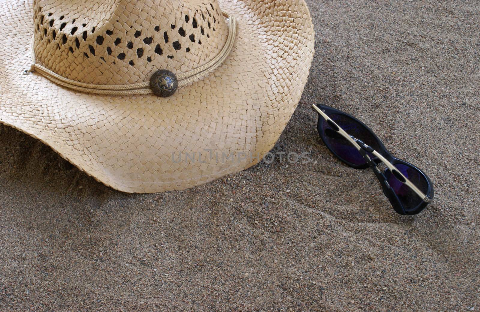 A hat and sunglasses are on the sand.