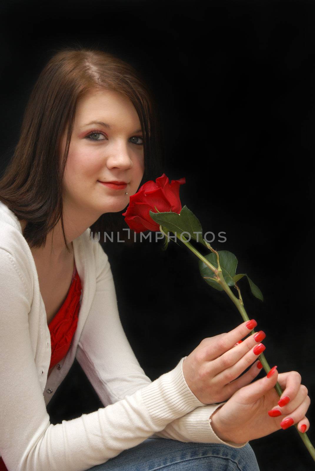 A woman holds a red rose close to herself.