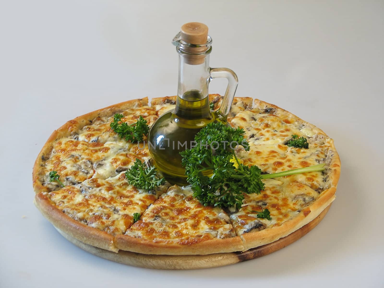 Pizza with a jug of oil and a bunch of greens in the center