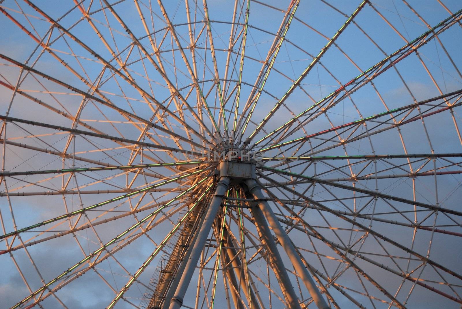 Center of ferris wheel. Spokes radiate outward, deep pink against blue sky
