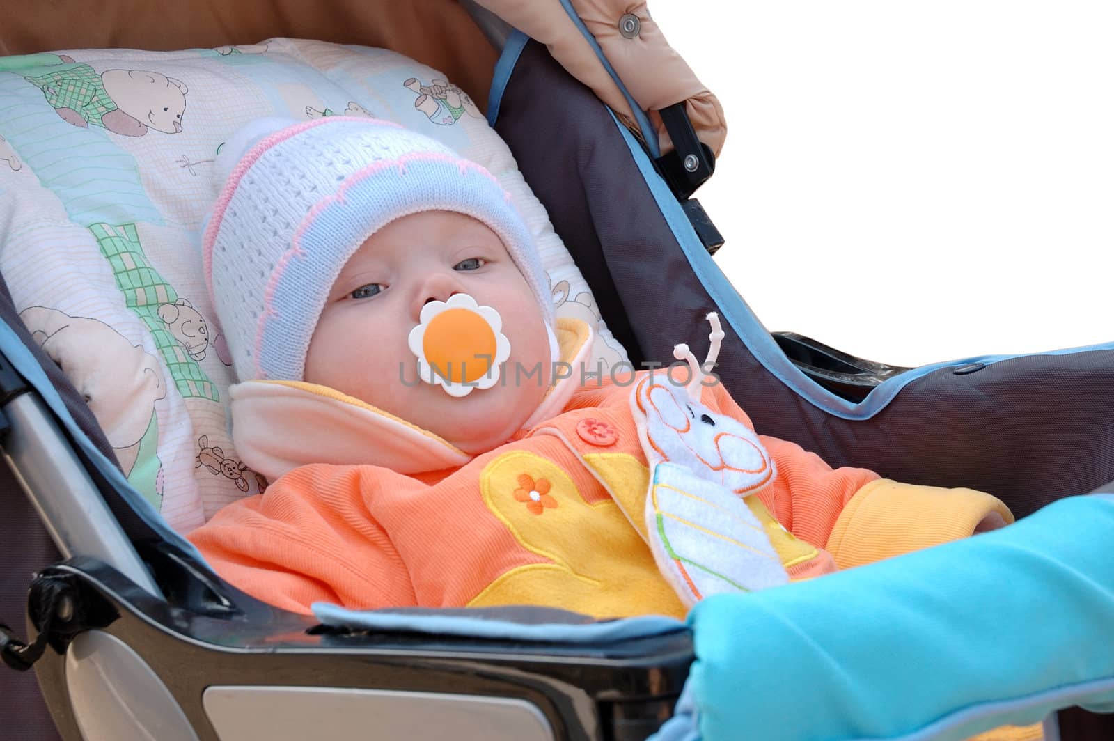 Little girl with baby's dummy sit in carriage. In cap and bright orange jacket.