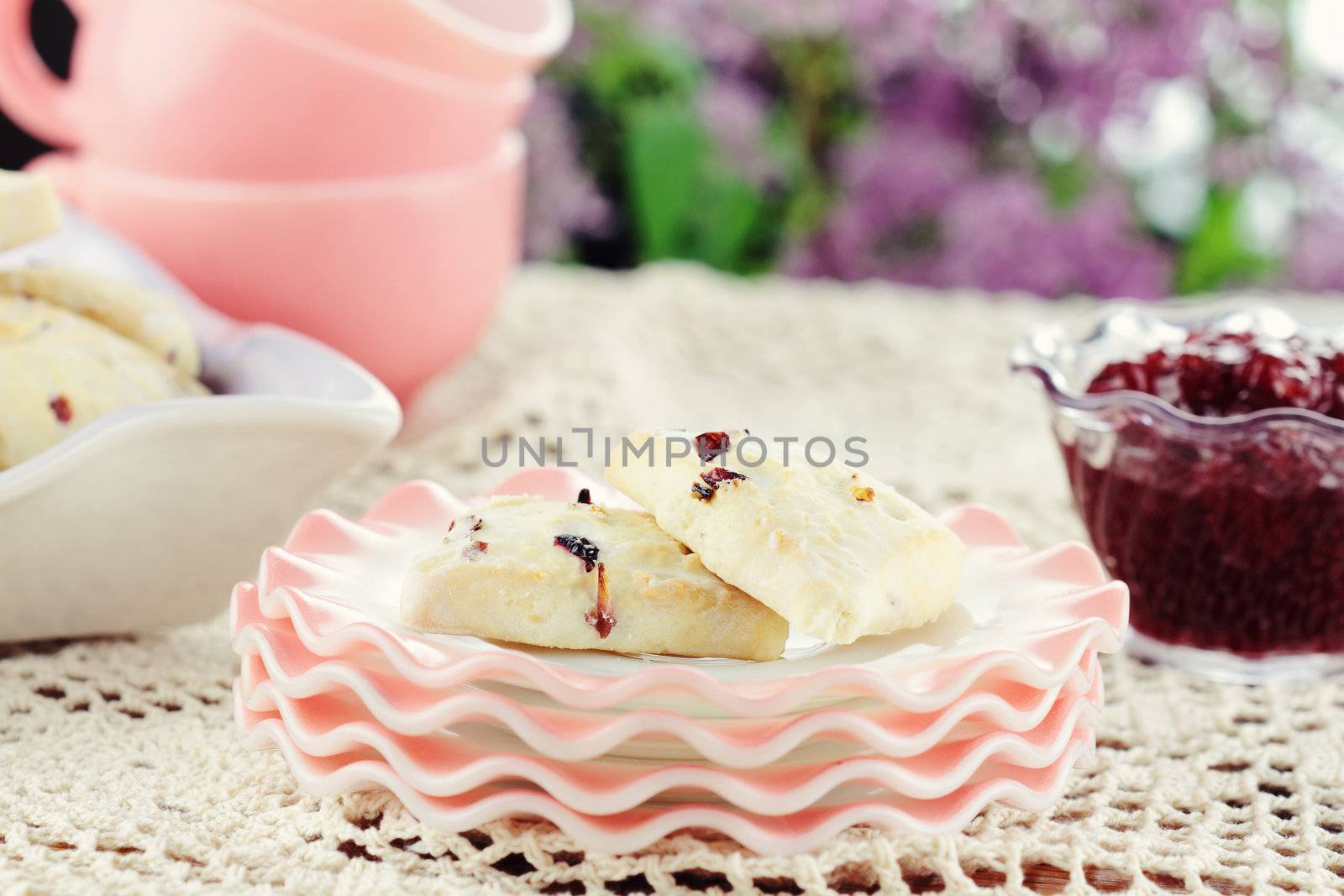 Closeup of freshly baked cranberry scones sitting on an outdoors table with strawberry preserves. Selective focus with shallow depth of field. 