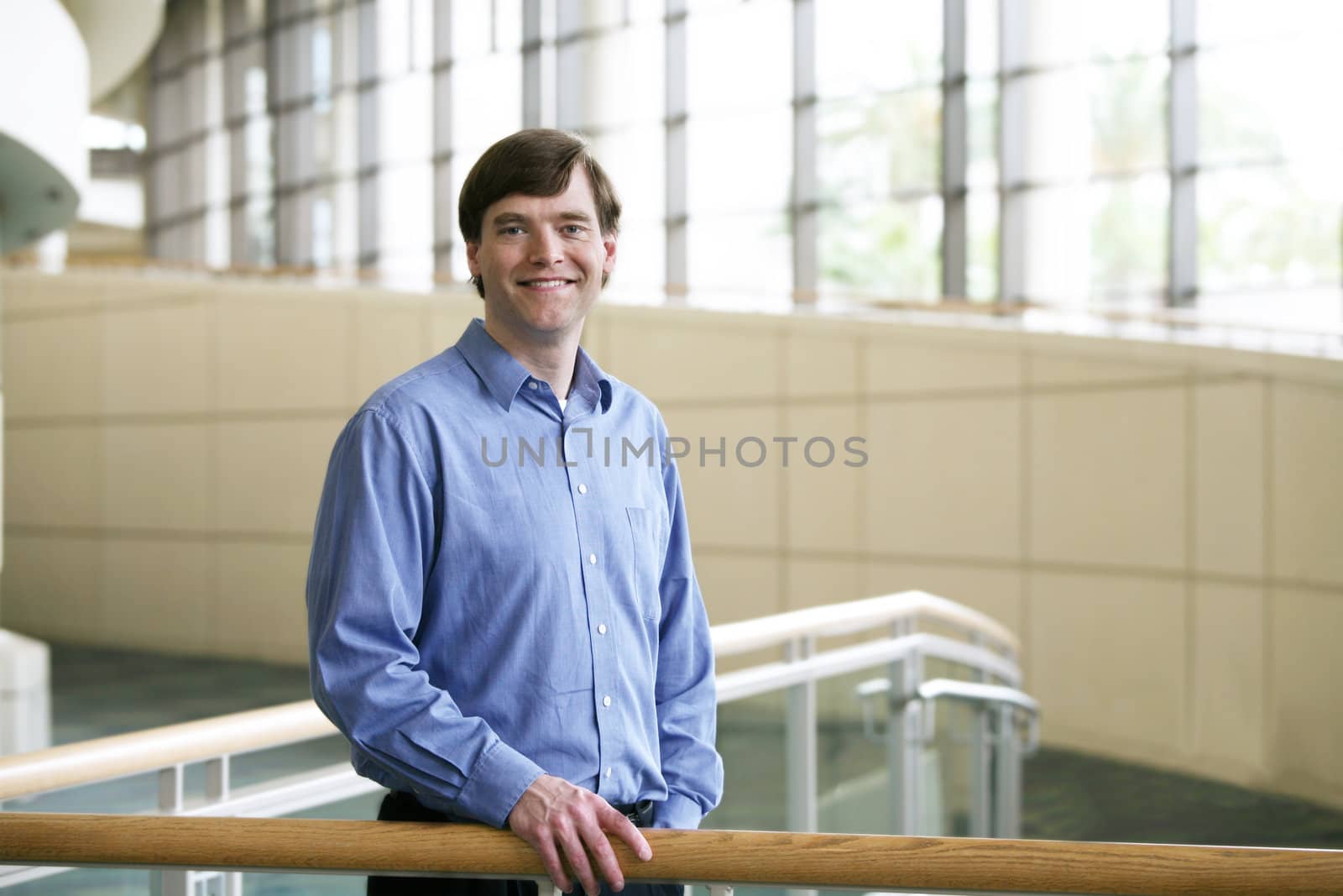 Handsome businessman leaning on railing in large office complex