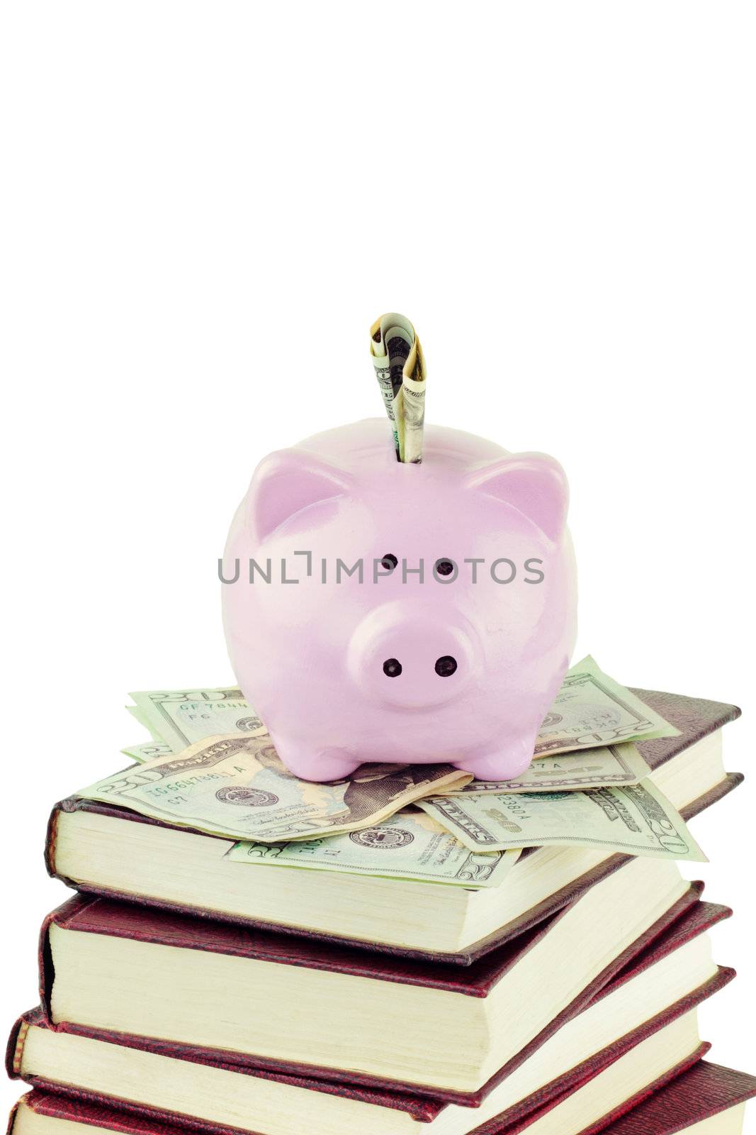 Ceramic piggy bank sitting on twenty dollar bills and a stack of books against a white background with copy space. 