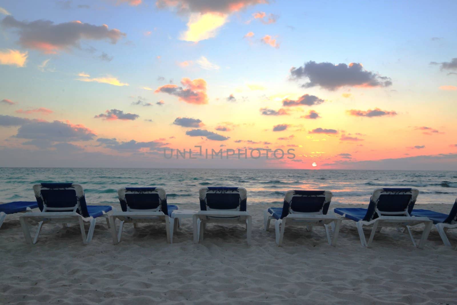 Sun rising over Mexican beach with lounge chairs.
