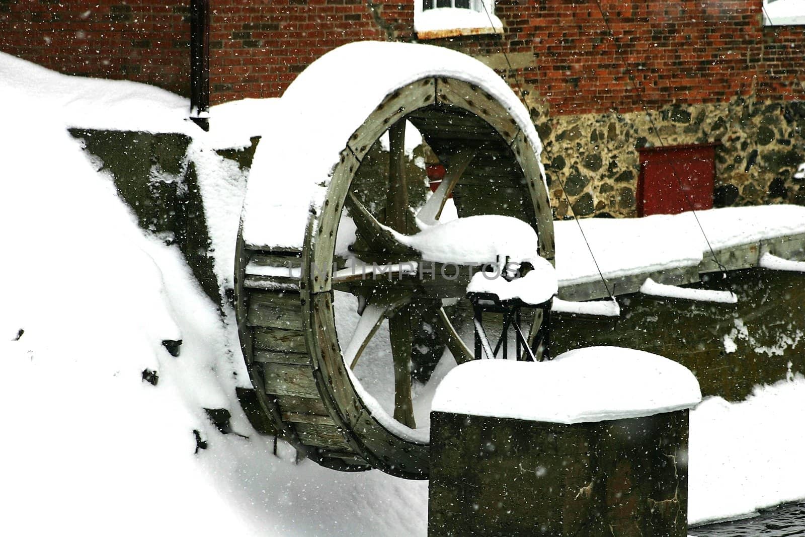 Snow covered wheel of watermill along river