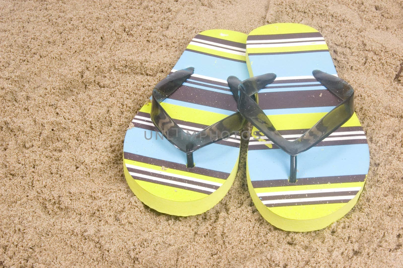 green colored summer slippers lying on sand