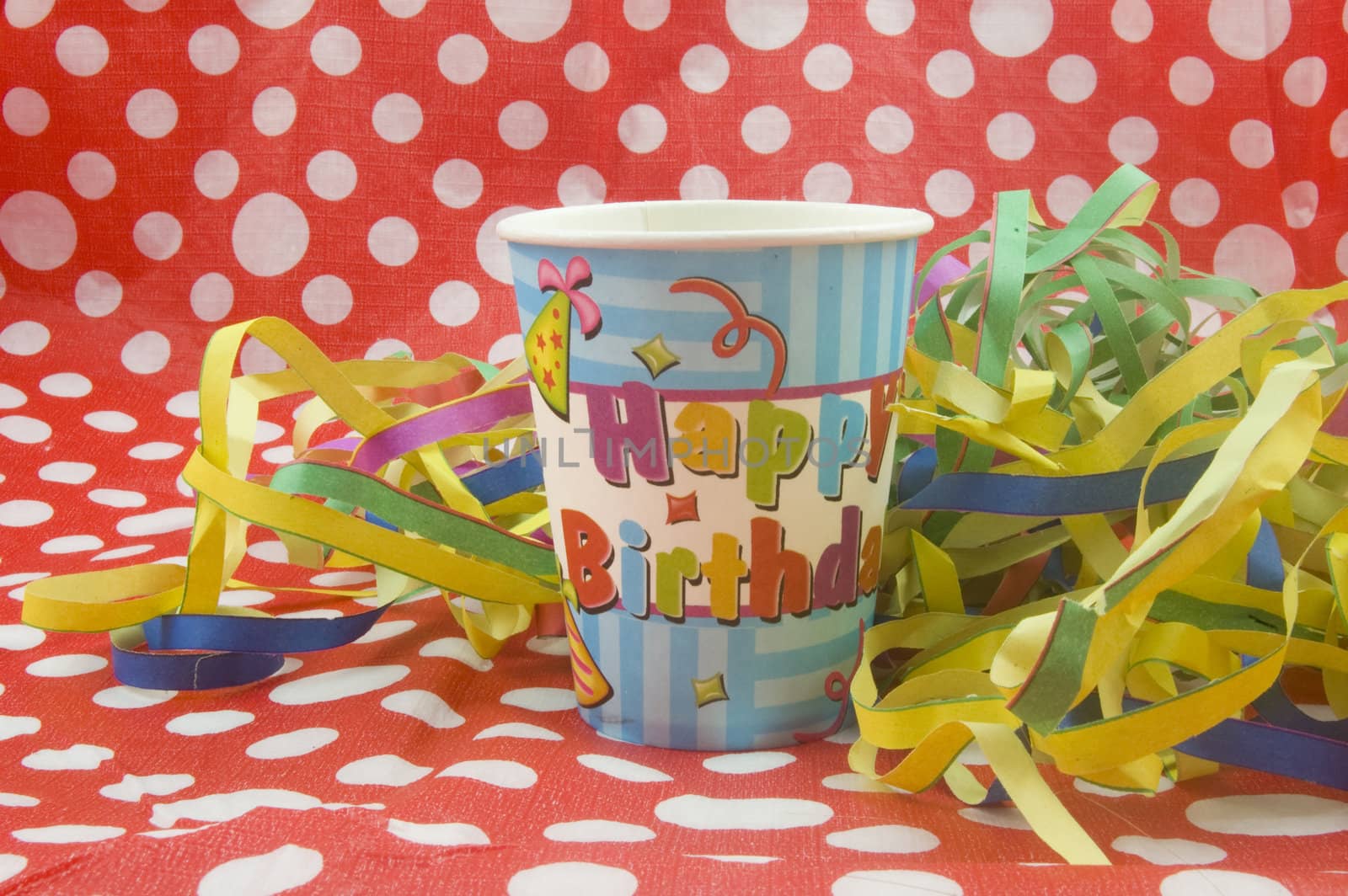 happy birthday cup with colorful streamers on red white dotted background