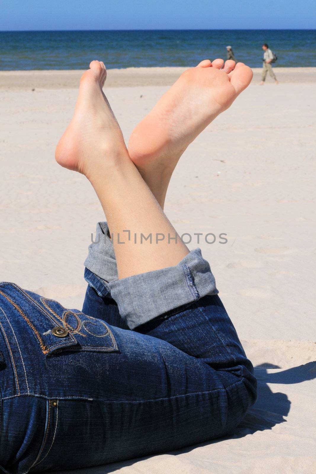 Woman in jeans with crossed legs resting on the beach
