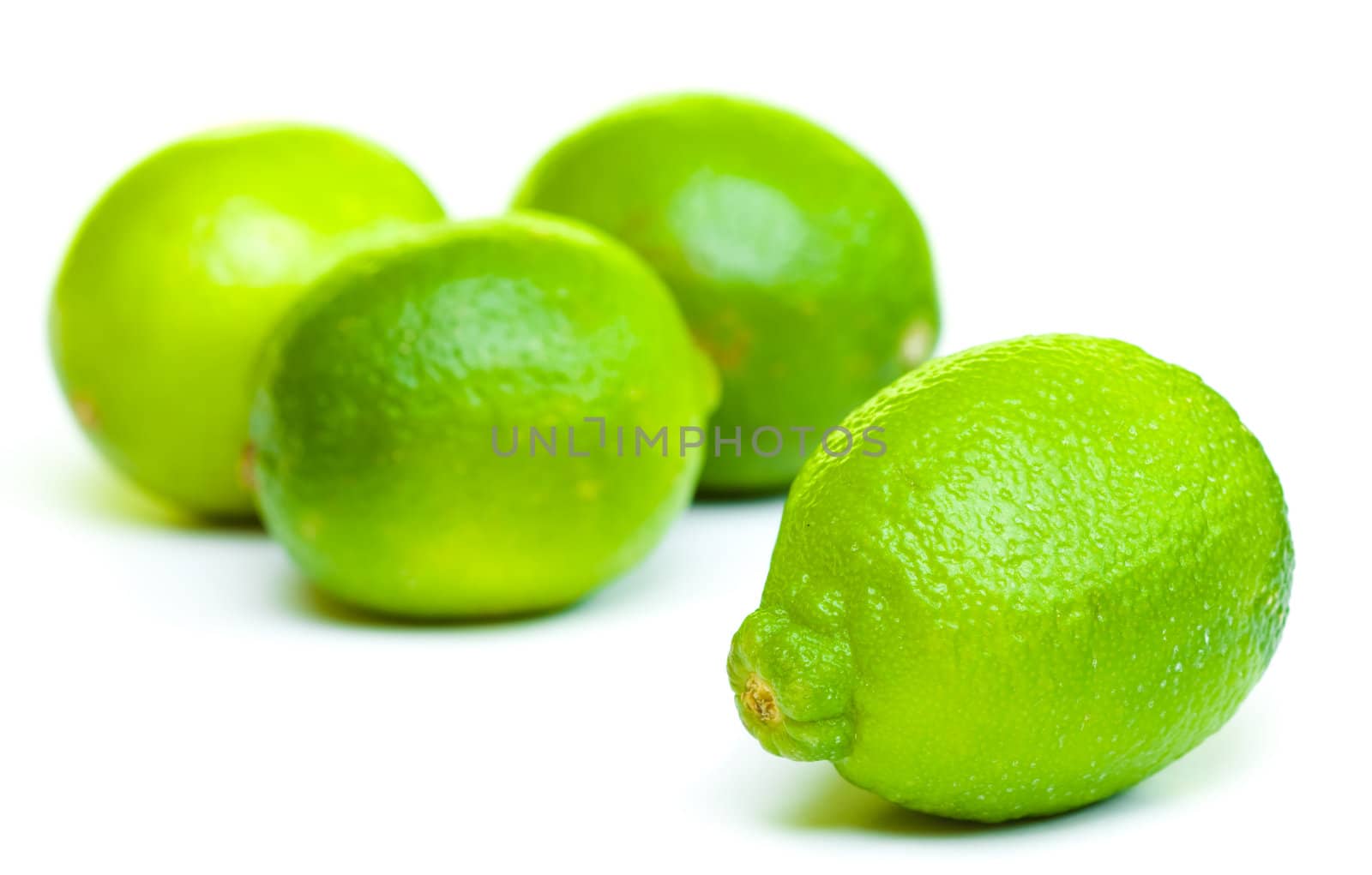 Limes on white background. Front lime is sharp detail and three limes at the background are out of focus