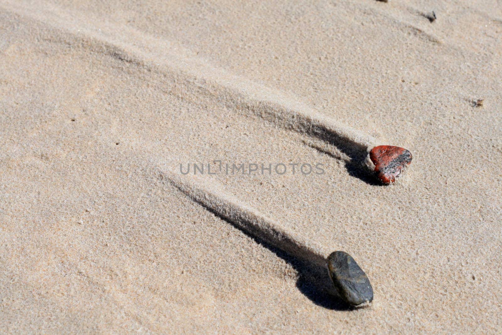 Two stones with a sand trail behind them caused by wind
