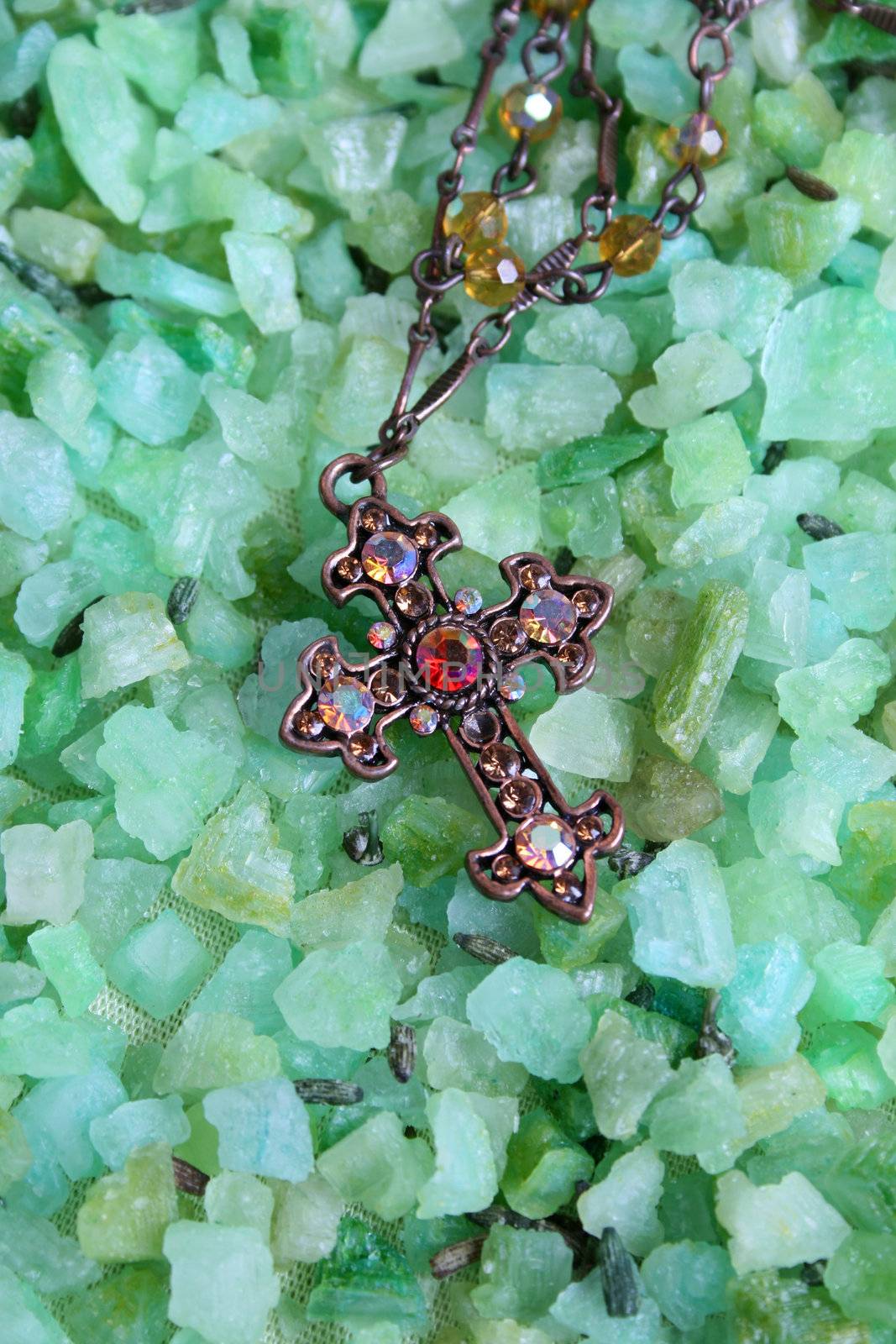 Cross shaped piece of jewelery on green bath crystals