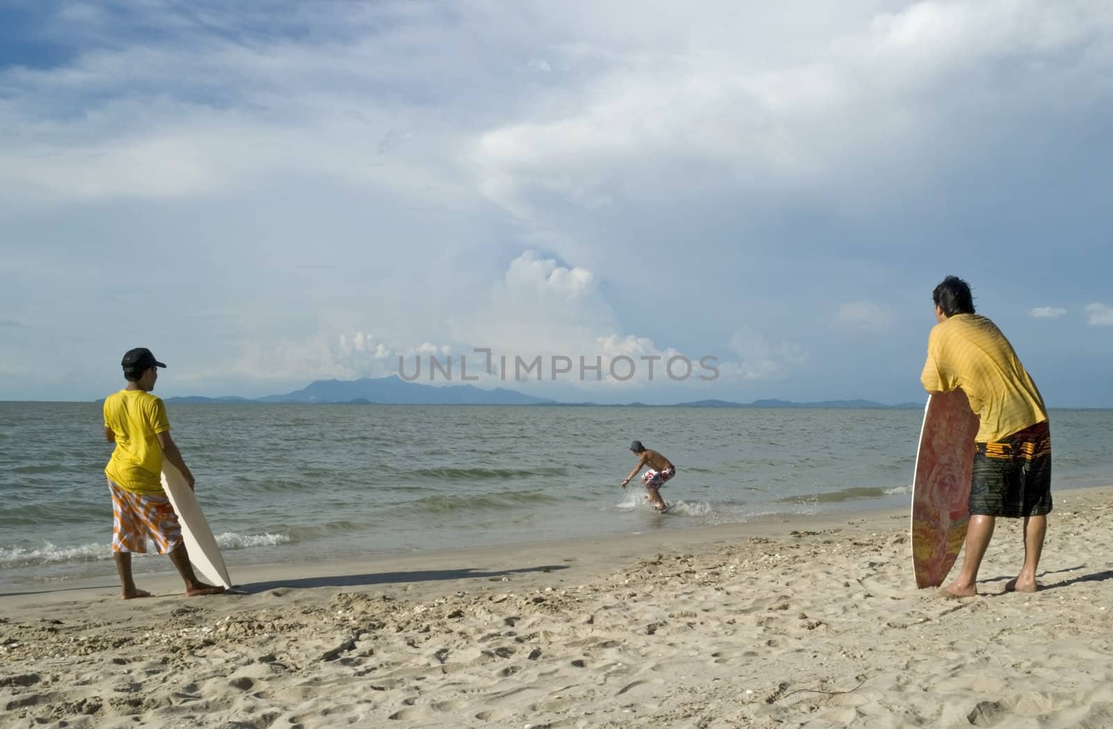A young man skin boarding at the beach while his friends look on. 
