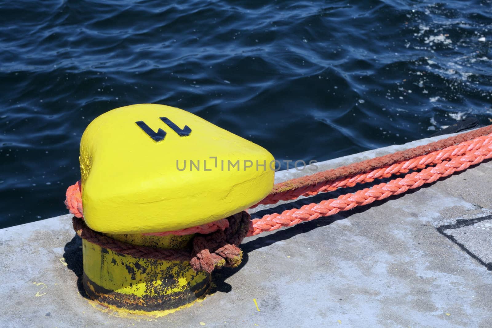 Yellow bollard mounted to the quay with ropes for mooring ships
