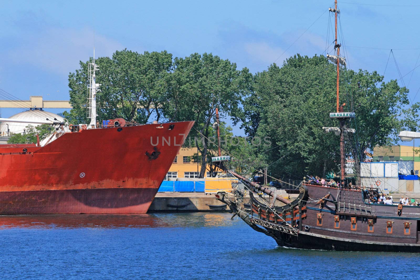 Cargo ship and pirate touristic ship passing together on the port channel
