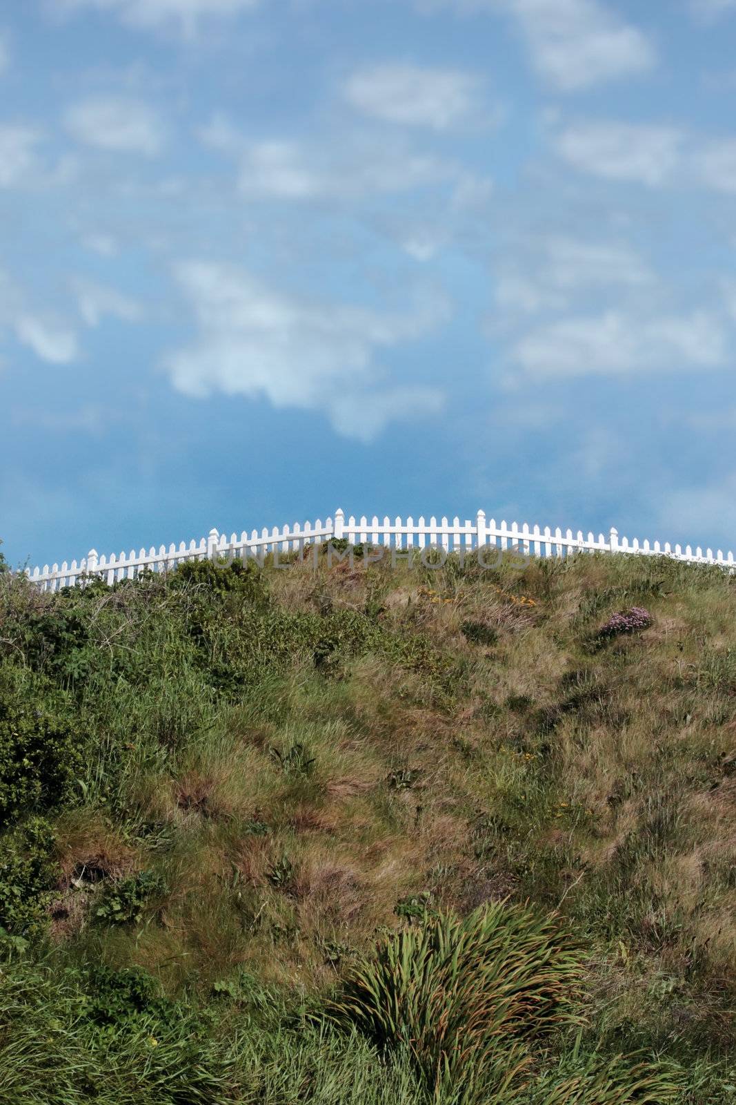 a white picket fence on top of a hill against a cloudy sky