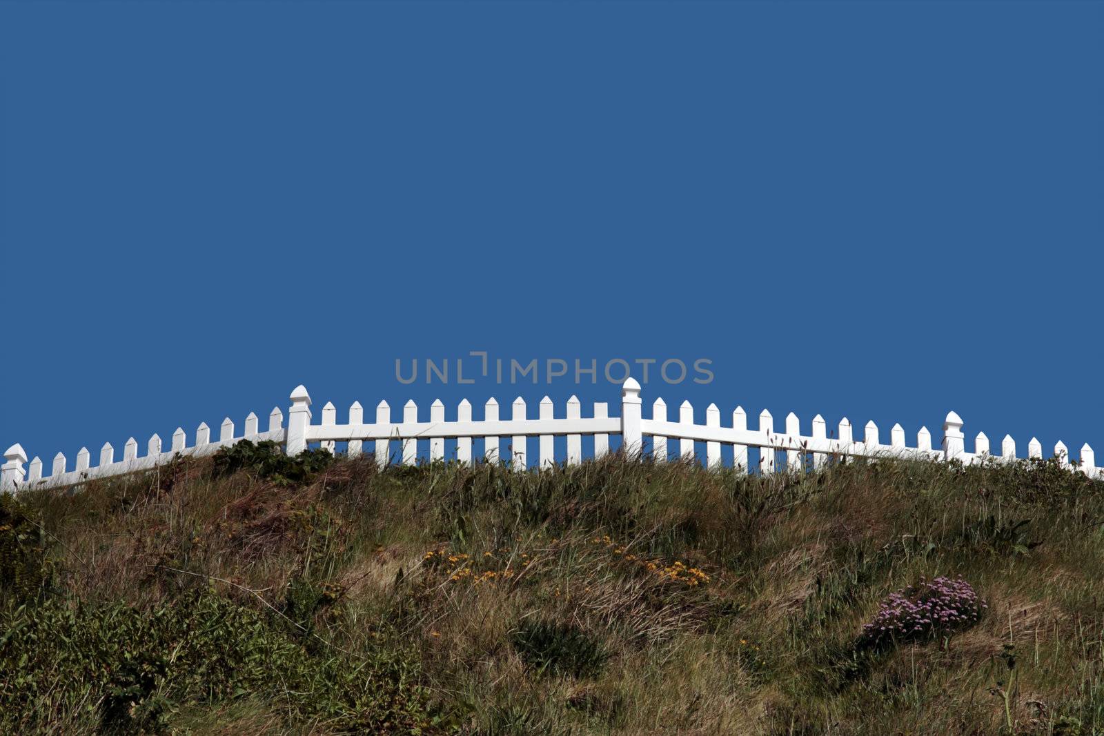 a white picket fence on top of a hill against a blue sky