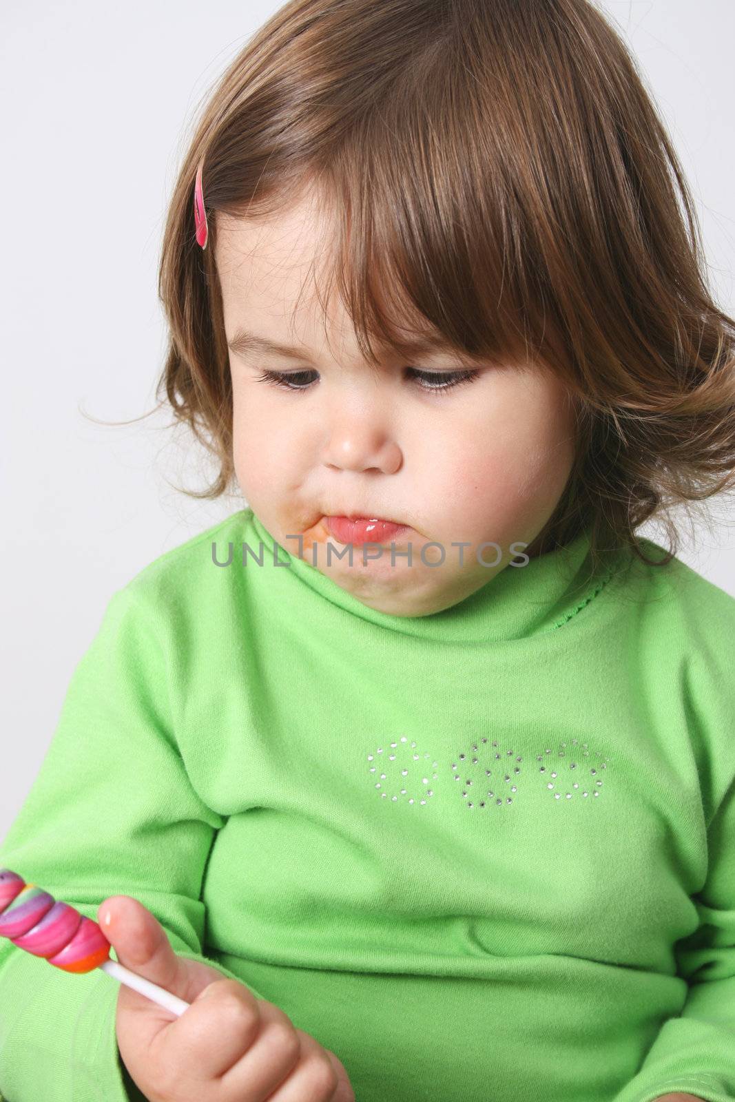 Toddler girl with chubby cheeks eating a sticky lollipop